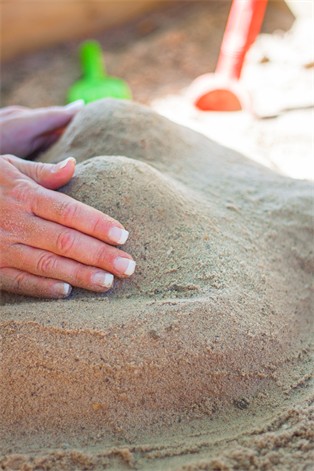 Zwei Frauenhände formen einen Körper beim Spielen im Sand. Foto: Sascha Becker