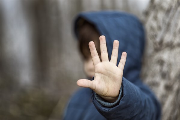 Ein Kind im Grundschulalter hält eine Hand vor sich als Abwehrhaltung