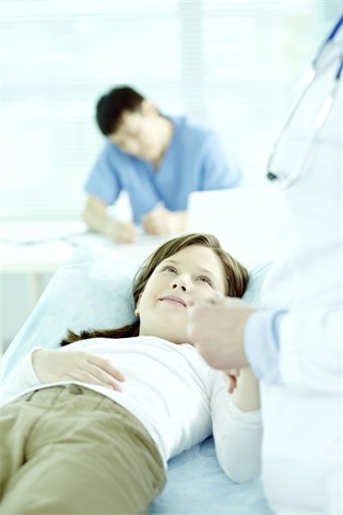 Patientin auf Untersuchungsliege blickt zum Arzt. Foto: mediaphotos iStock